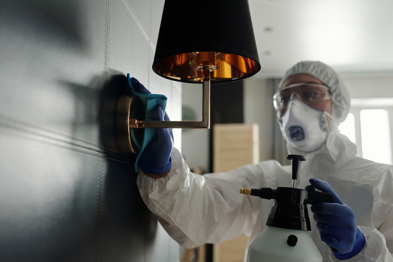 Services-01 A person wearing protective gear sanitizes a wall lamp to prevent virus spread.
